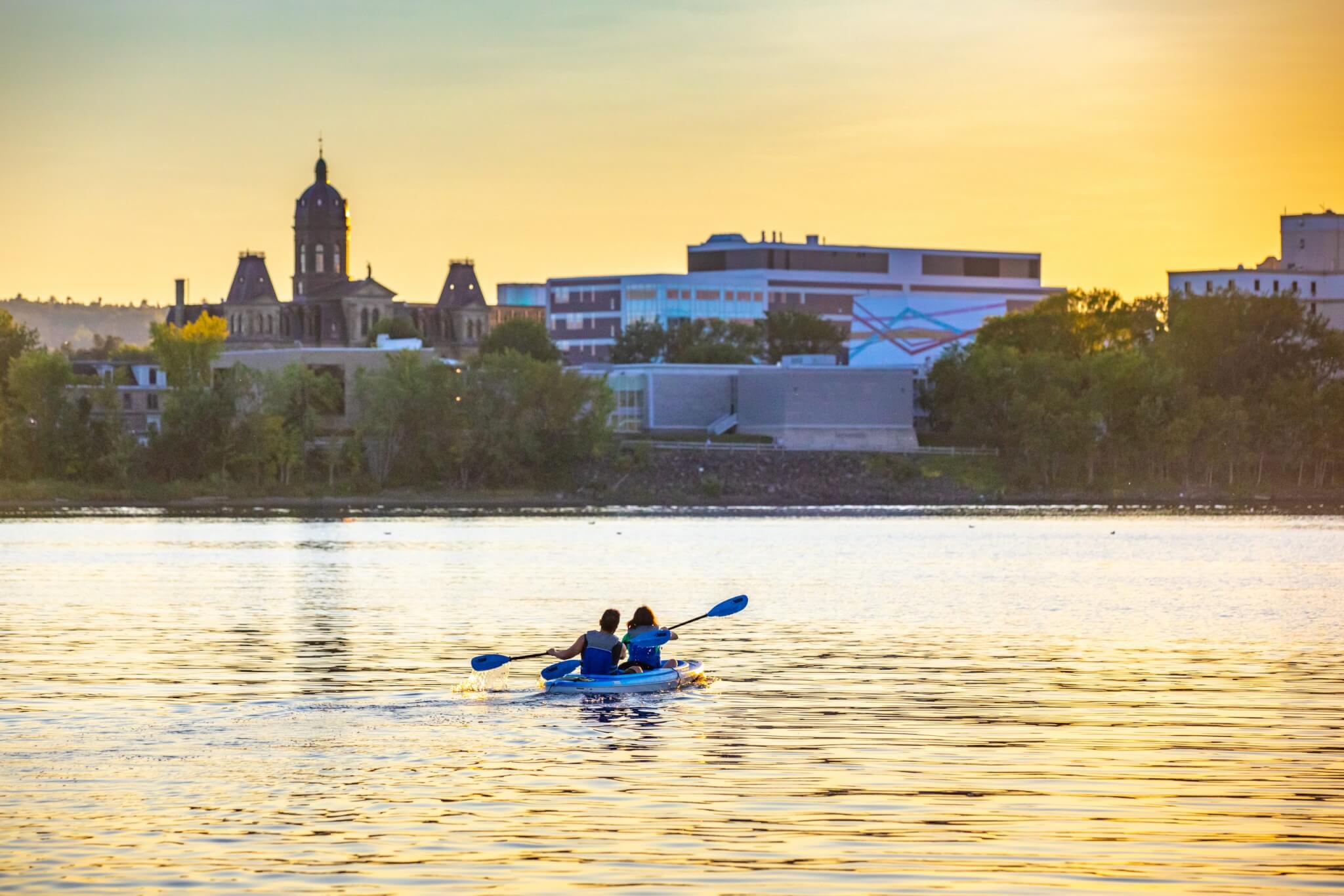 Two people paddling together across the Saint John river at sunset.